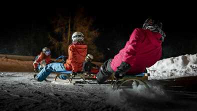 Eine Gruppe von Leuten macht eine Nachtrodelbahn in St. Anton Eine Gruppe von Leuten macht eine Nachtrodelbahn in St. Anton
