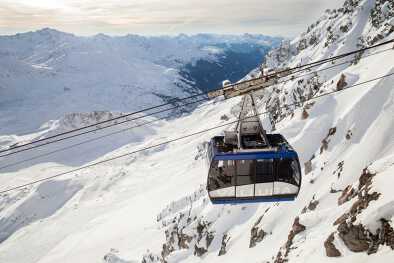 Die Seilbahnkabine der Valluga mit Touristen gegen verschneite Klippen Die Seilbahnkabine der Valluga mit Touristen gegen verschneite Klippen