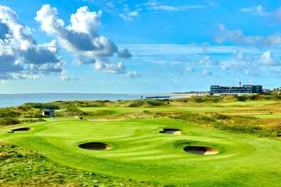 Green golf course with round bunkers with a hotel and the sea in the background
Green golf course with round bunkers with a hotel and the sea in the background