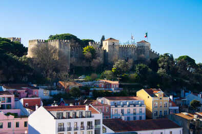 Una vista attraverso gli edifici colorati, i tetti e i giardini di Lisbona, Portogallo, verso l'imponente Castelo de S. Jorge (Castello di San Giorgio) in una giornata di sole. Una vista attraverso gli edifici colorati, i tetti e i giardini di Lisbona, Portogallo, verso l'imponente Castelo de S. Jorge (Castello di San Giorgio) in una giornata di sole.