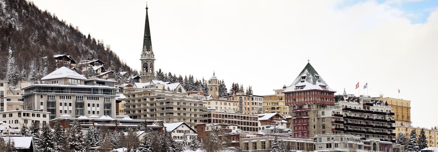 Skyline of St Moritz in Switzerland with several houses and clock house in winter with snow