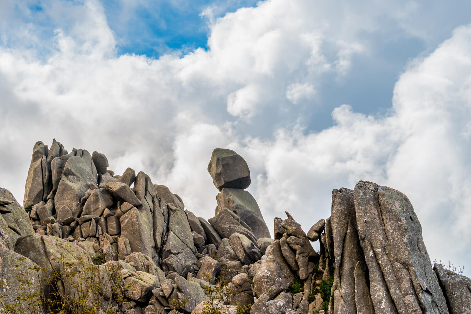 Closeup view of Omu di Cagna (Uomo di Cagna) on the island of Corsica. The granite rock is balanced at the top of a peak on the mountain of Cagna, surrounded by dramatic clouds and blue sky.