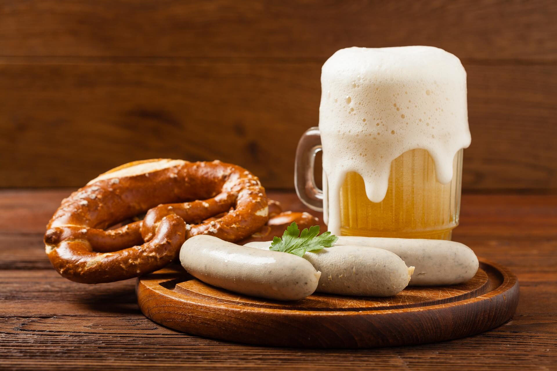 Boiled white sausages, served with beer and pretzels. Perfect for Octoberfest. Natural wooden background. Front view.
