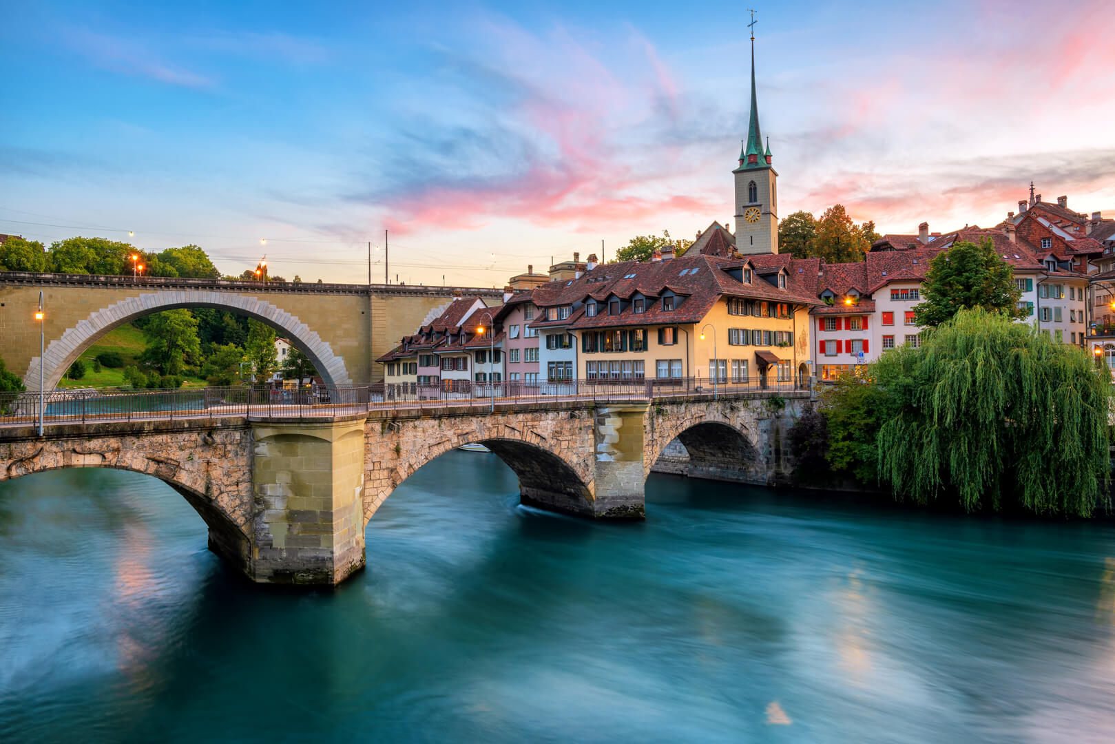 Historical Old Town of Bern city, tiled roofs, bridges over Aare river and church tower on dramatic sunset, Switzerland