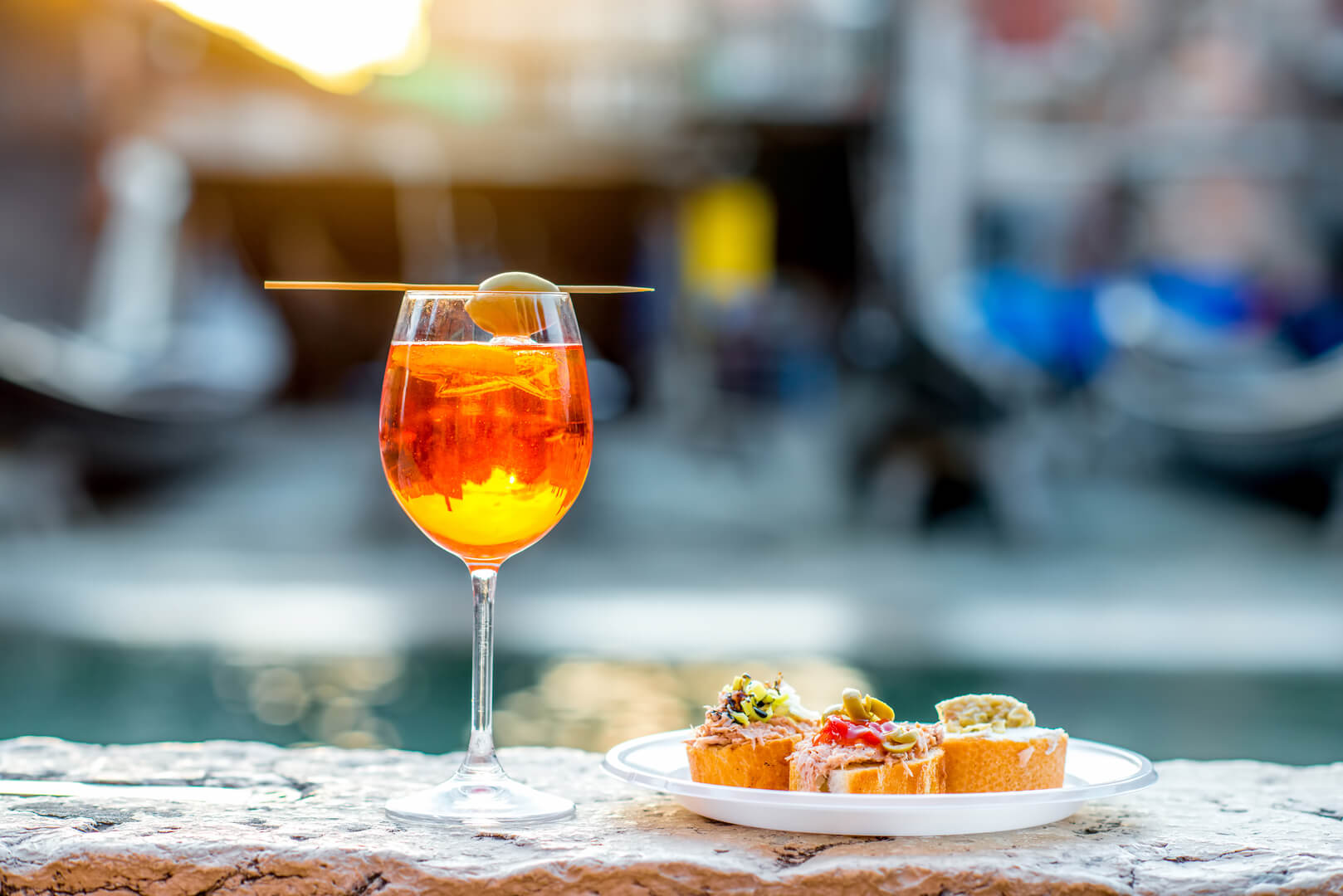 Spritz Aperol drink with venetian traditional snacks cicchetti on the water chanal background in Venice. Traditioanal italian aperitif. Image with small depth of field.