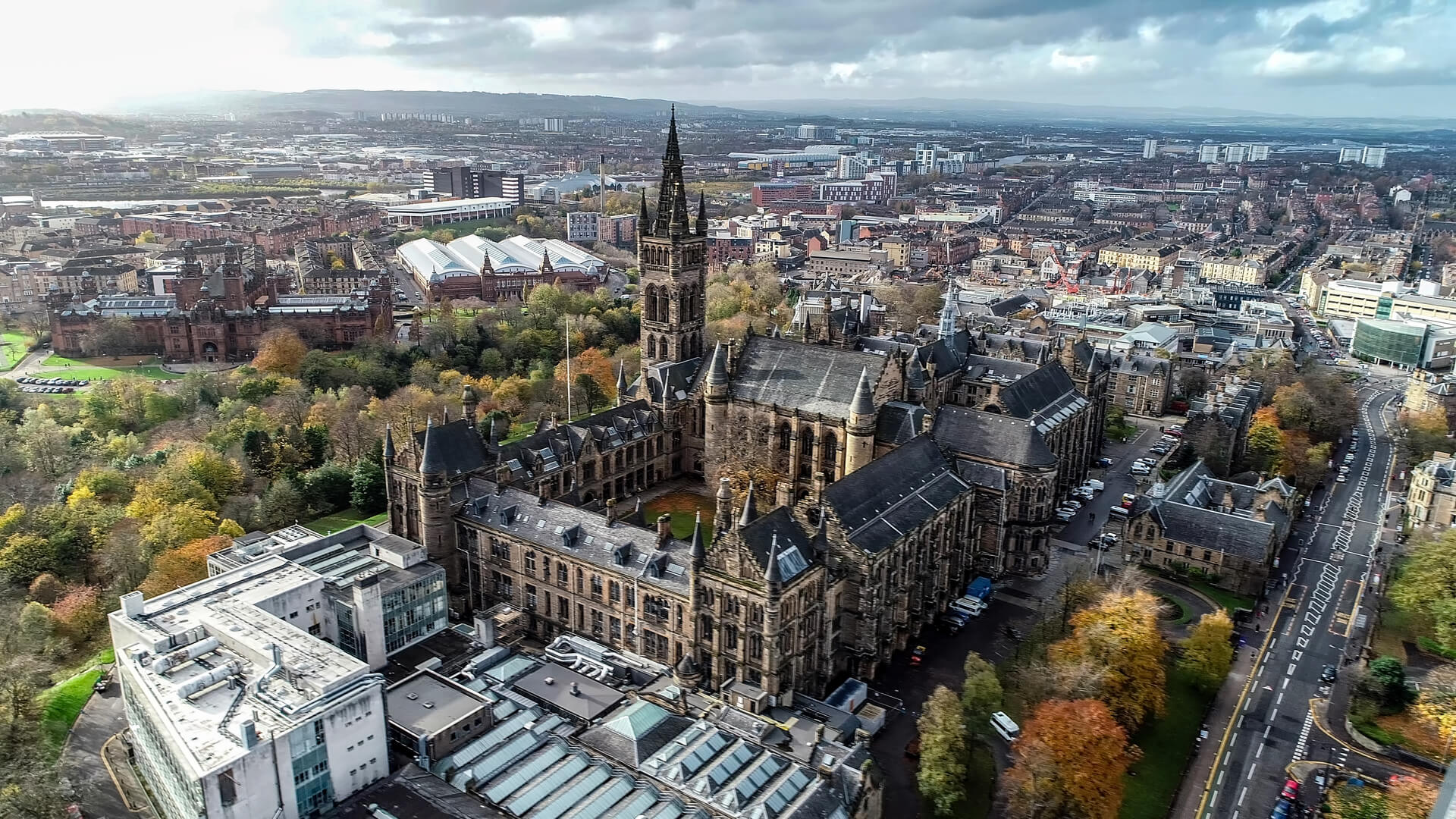 Low level aerial image over the autumn foliage of trees in Kelvingrove Park, Glasgow, to the gothic tower of Glasgow University with the cityscape behind.
