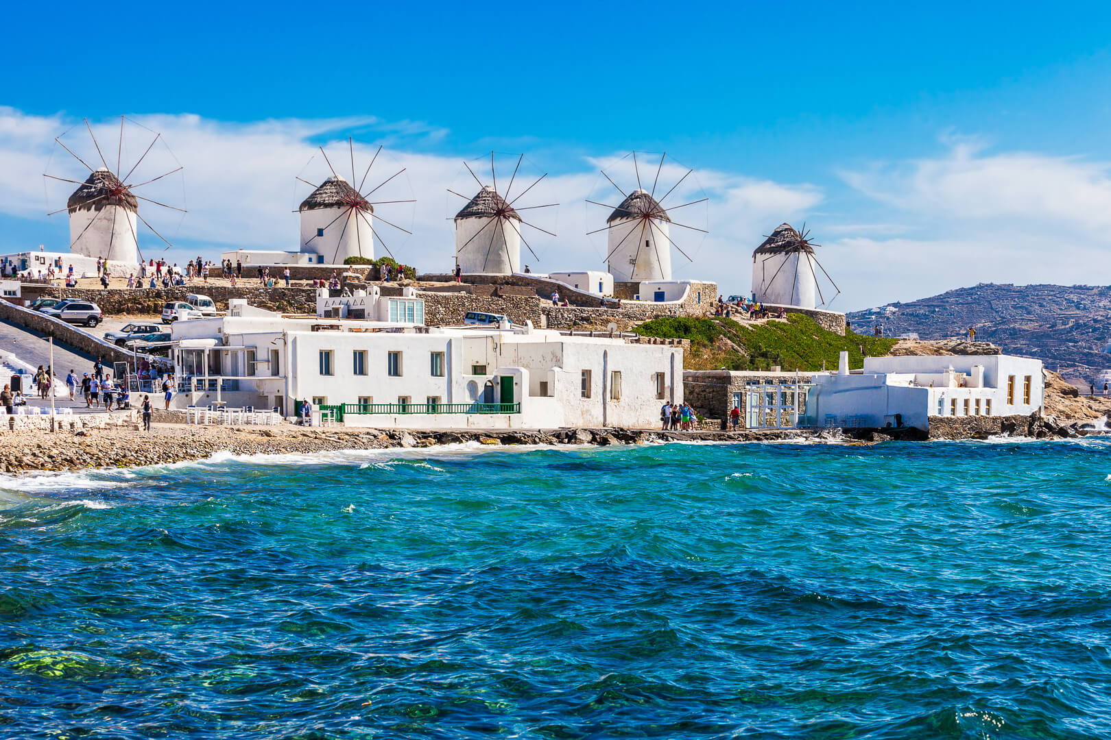 Вид на легендарные ветряные мельницы в ясный и яркий летний солнечный день вдоль синего моря и побережья Миконоса, Греция