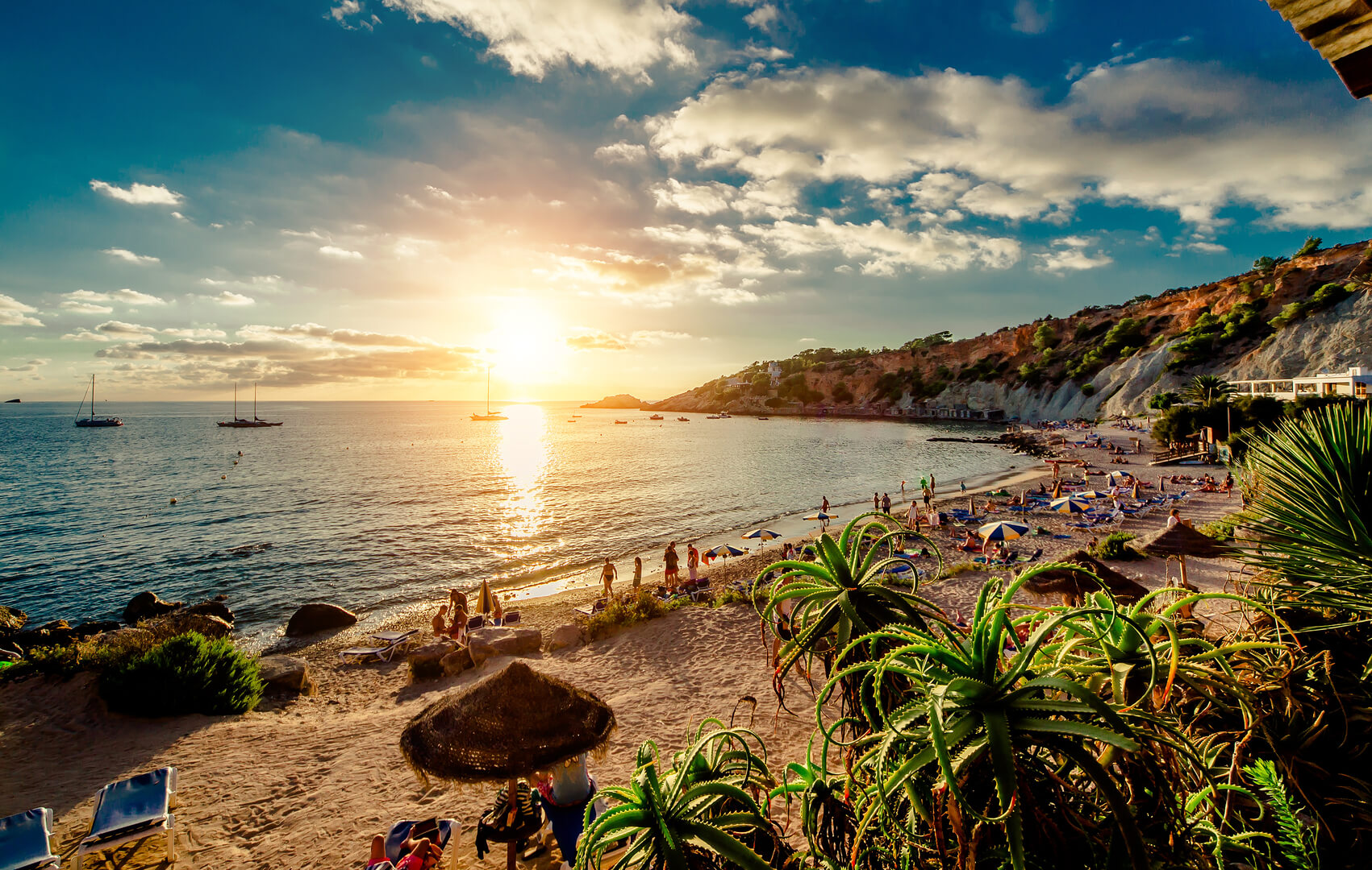 Plage de Cala d'Hort au coucher du soleil. Les gens se font bronzer, font la fête sur la plage rocheuse pittoresque tropicale de sable pendant le coucher du soleil. Cette plage est très appréciée des clubbers et des vacanciers des Baléares. Ibiza