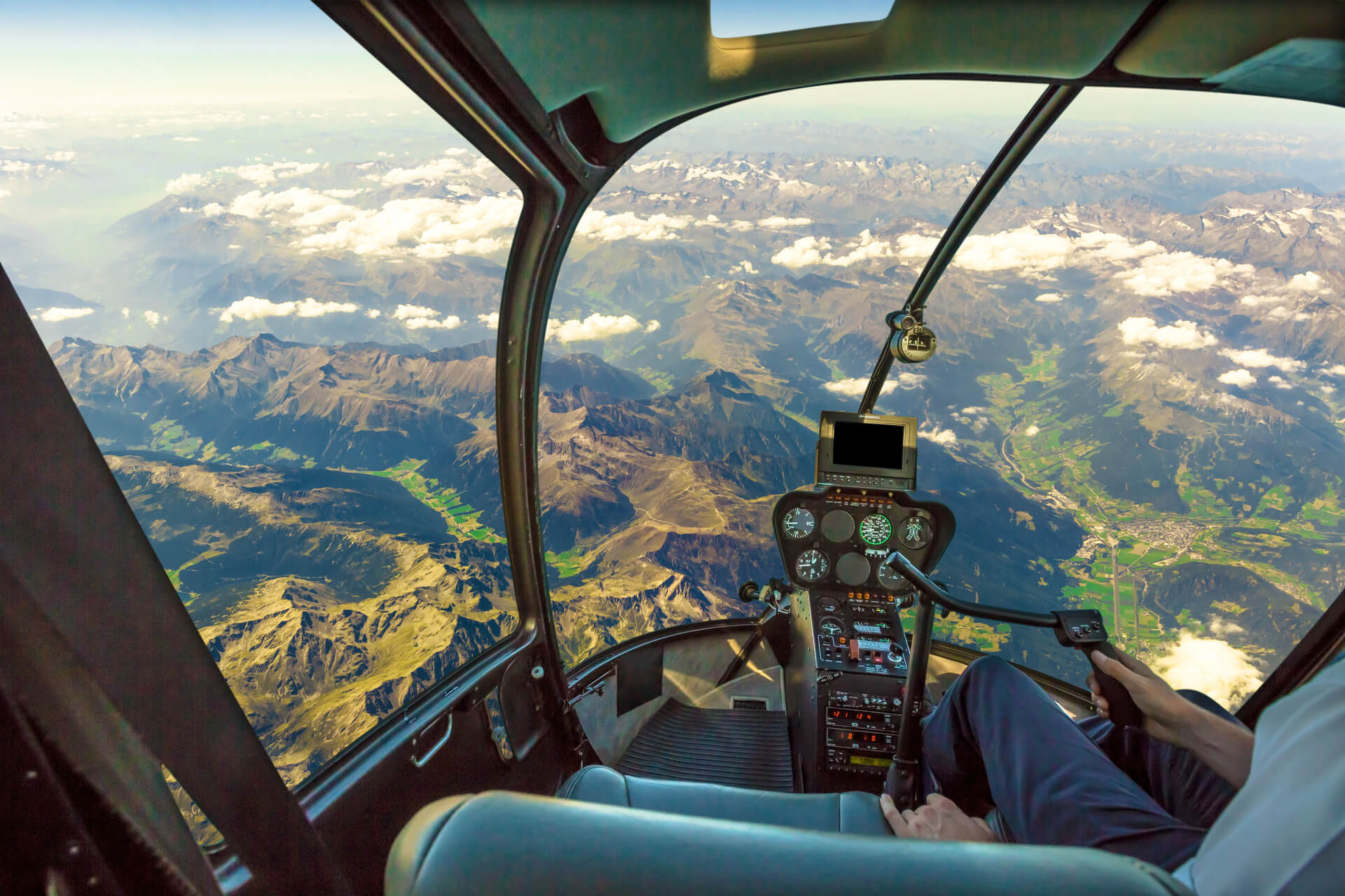 Cockpit d'hélicoptère volant sur un paysage de montagne et un ciel nuageux, avec le bras du pilote conduisant dans la cabine. Vue aérienne spectaculaire des Alpes.