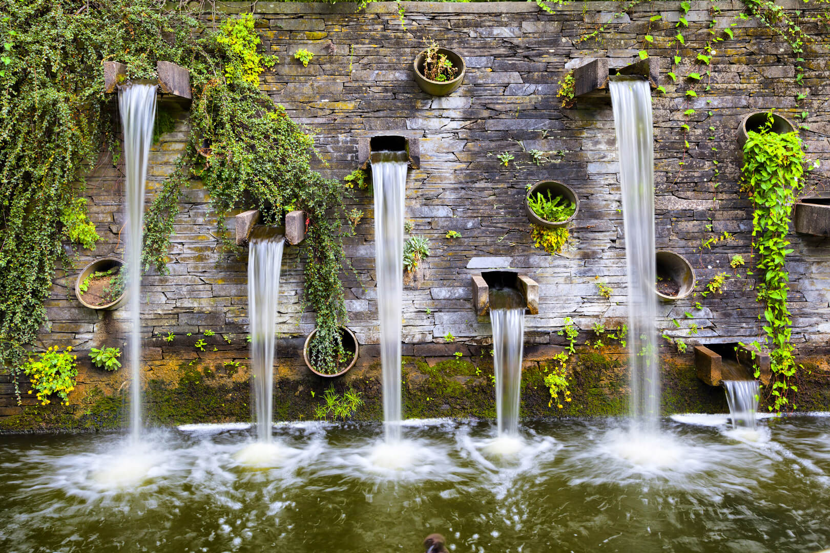 Скальная стена с небольшими водопадами в парке Planten un Blomen в Гамбурге, Германия