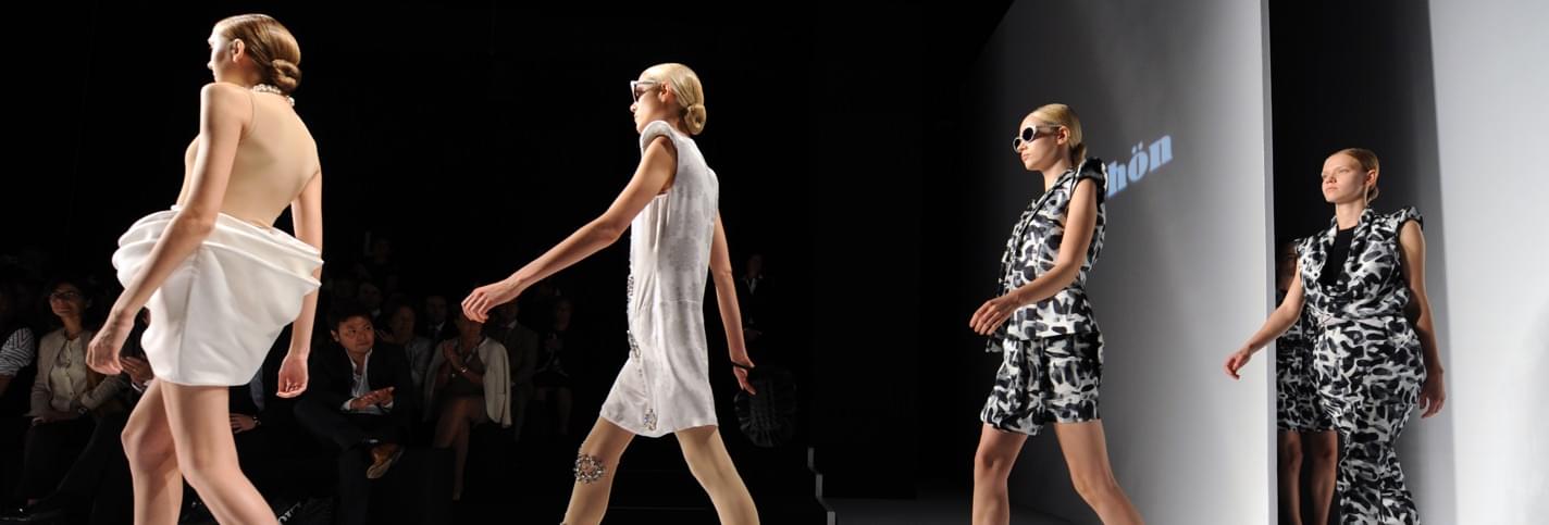 Quatre top-modèles défilant à la Fashion Week Milan avec des spectateurs dans le fond