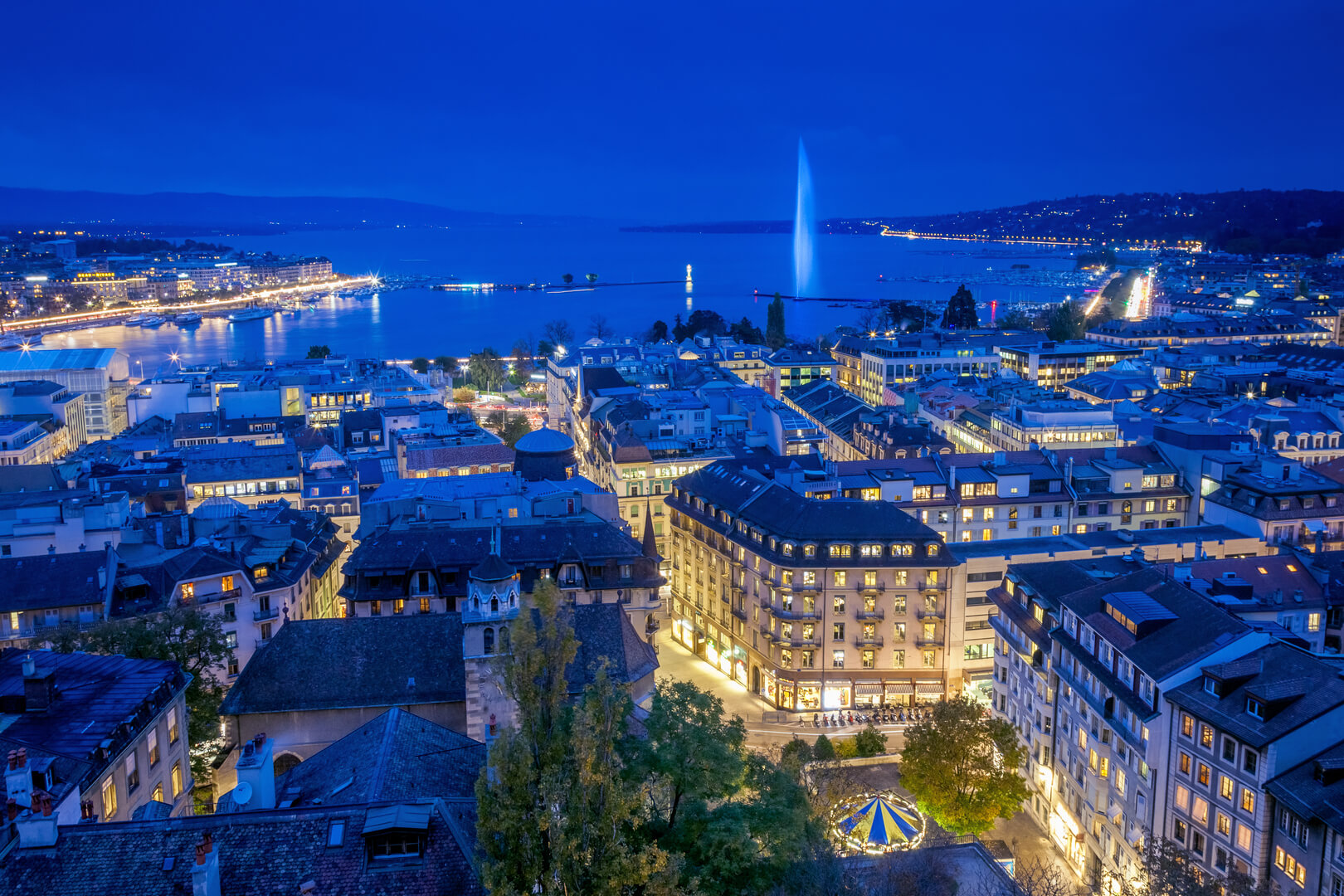 Vue aérienne du centre ville de Genève et du Jet d'eau de nuit lors de la Journée mondiale du diabète. Cette photo a été prise peu après le coucher du soleil, à l'heure bleue, depuis le sommet de la tour de la cathédrale Saint-Pierre.