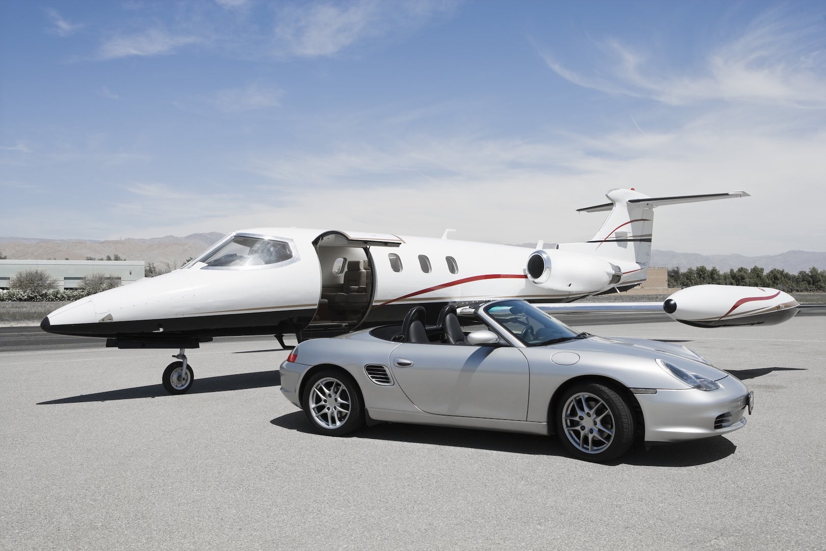 Private jet with open door and Porsche at the airport.