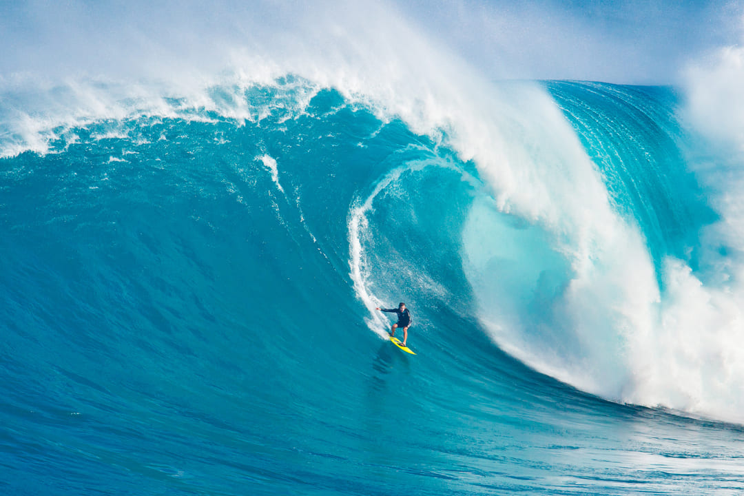 Ein professioneller Surfer reitet eine 5-Meter-Röhrenwelle an einem hawaiianischen Strand.