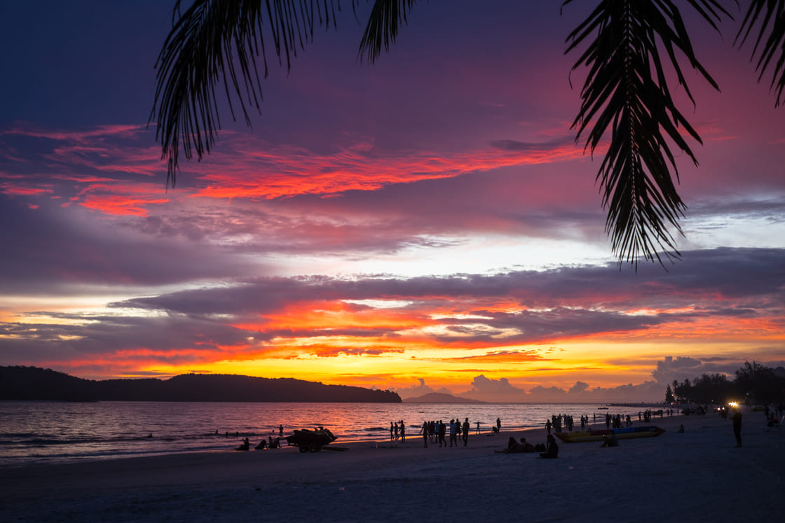 Vor dem Strand von Cenang beobachten die Menschen den Sonnenuntergang in rosa und orangefarbenen Tönen.