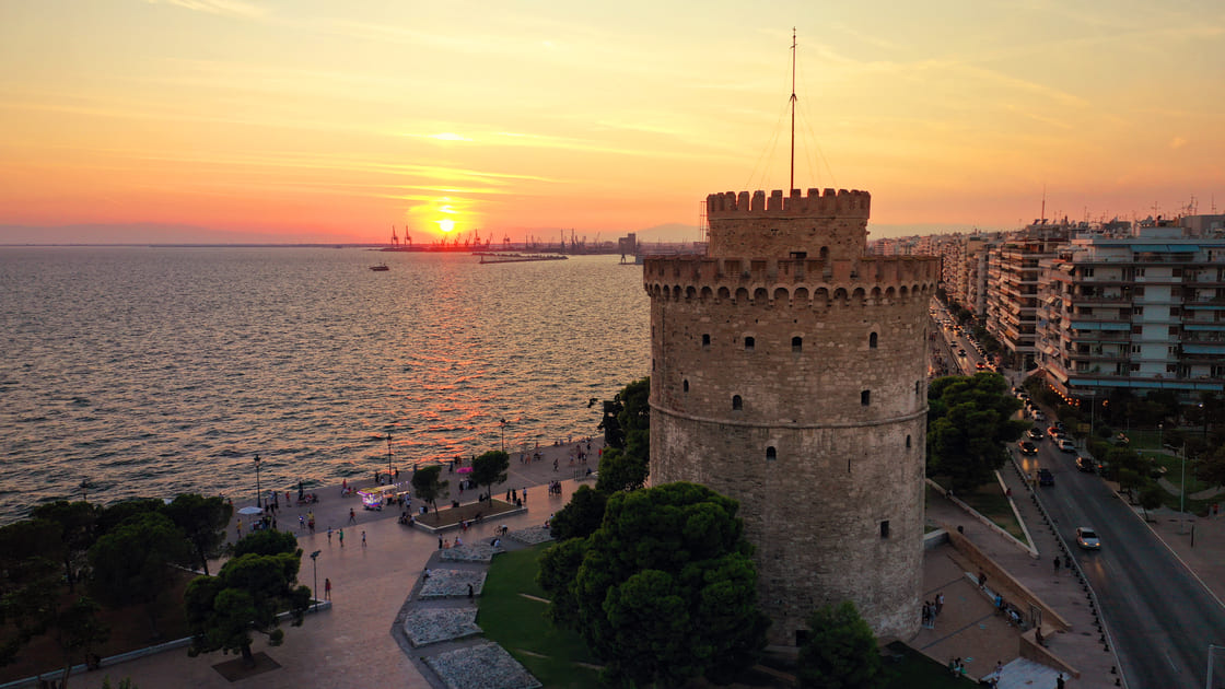 Drohnenansicht des historischen Wahrzeichens - der alte byzantinische Weiße Turm von Thessaloniki oder Saloniki bei Sonnenuntergang mit goldenen Farben, Nordgriechenland