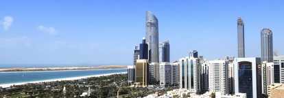 Blick auf Abu Dhabi mit Skikratzern rechts und Bäumen und dem Meer bei Tag