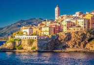 Le phare de Bastia et ses maisons colorées avec la mer et les montagnes en arrière-plan.