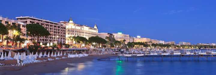 A private beach in Cannes by night with the illuminated Intercontinental Carlton palace on the Croisette