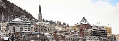 Skyline of St Moritz in Switzerland with several houses and clock house in winter with snow