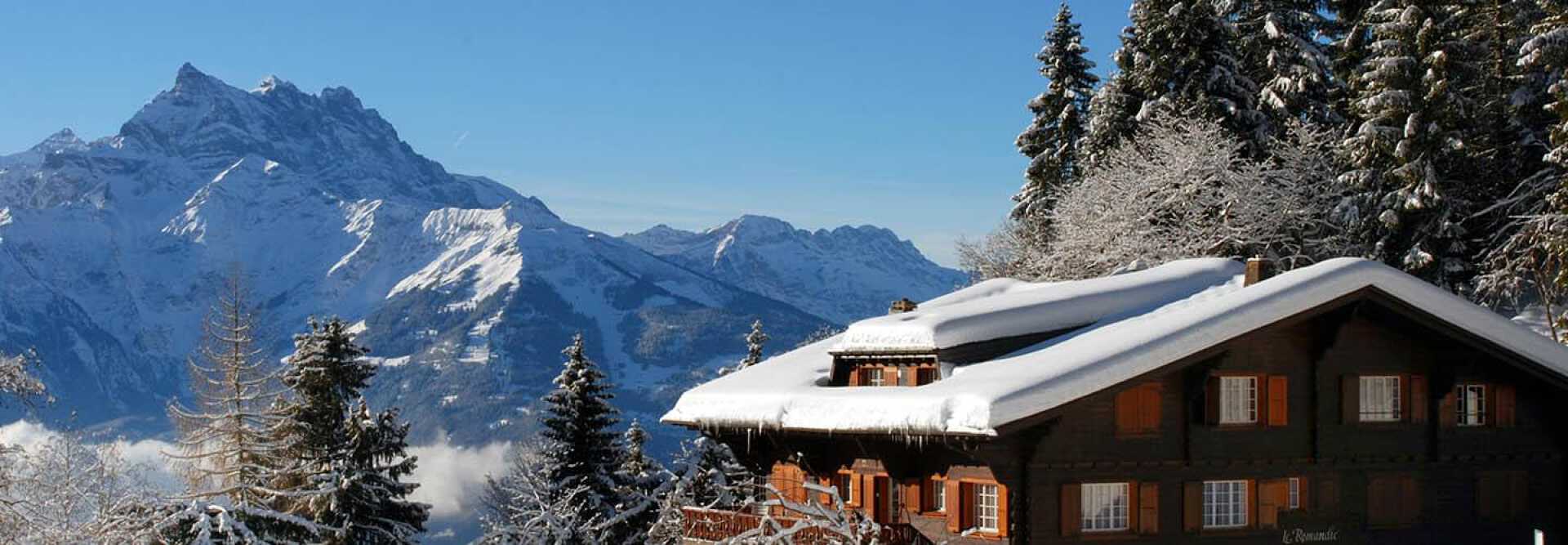On the right is a chalet with a snow-covered roof, in the distance on the left are the mountains. Villars, Switzerland.