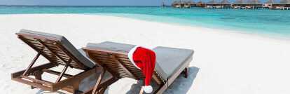 Wooden deckchairs on the beach sand in the bahamas with christmas beanie cap and background sea
