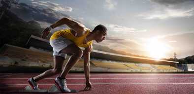 Focused Afro-American sprinter with grey trunks and yellow undershirt with bleachers in the background