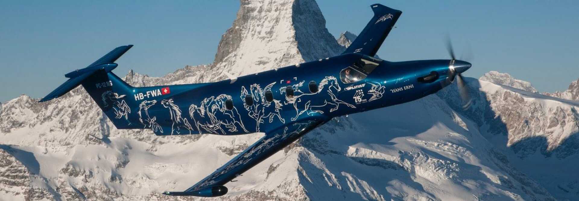 Blue Pilatus PC-12 turboprop with white drowing flying over Swiss snowy mountains