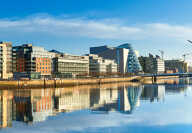 Modern buildings and offices on Liffey river in Dublin on a bright sunny day, bridge on the right is a famous Harp bridge.
