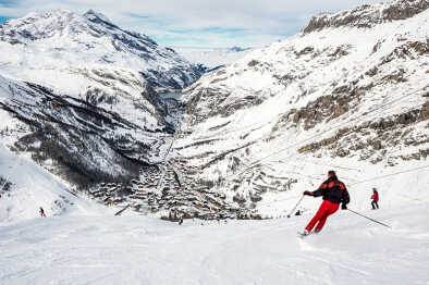Skifahrer auf der Piste mit dem Dorf Val d'isere im Hintergrund. Der Skifahrer ist Bewegungsunschärfe. Val d'isere, Frankreich