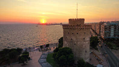 Aerial drone view of iconic historic landmark - old byzantine White Tower of Thessaloniki or Salonica at sunset with golden colours, North Greece
