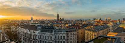 Luftaufnahme der Dächer von Wien in Österreich bei Sonnenuntergang. Im Hintergrund eine Kathedrale