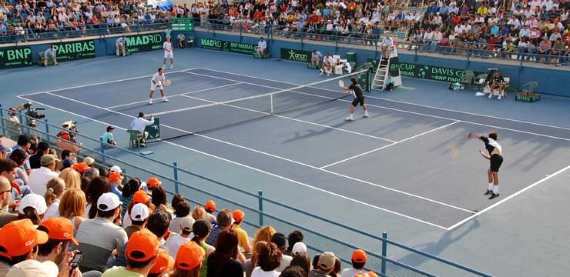 Doubles match at the Davis Cup with the blue tennis court and spectators wearing orange cups