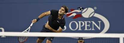 Roger Federer in black polo and blue shorts serving at the New York Open Tennis Championship