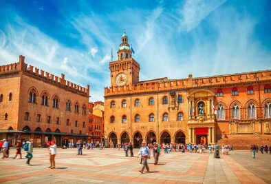 Italia Piazza Maggiore a Bologna vecchia torre del municipio con grande orologio e cielo blu sullo sfondo. Edifici antichi gallerie di terracotta