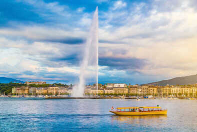 Vue panoramique de la ligne d'horizon de Genève avec la célèbre fontaine du Jet d'Eau et le bateau traditionnel dans le quartier du port, dans la belle lumière du soir au coucher du soleil, canton de Genève, Suisse.