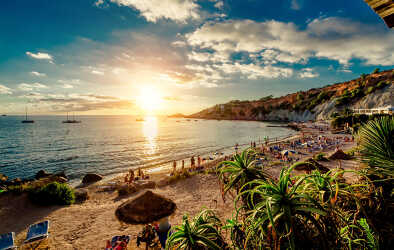 Cala dHort Strand bei Sonnenuntergang. Menschen sonnenbaden, haben eine Partei auf dem sandigen tropischen malerischen felsigen Strand während des Sonnenuntergangs. Dieser Strand ist sehr beliebt für Clubber und Urlauber Balearen. Ibiza
