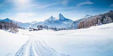 Панорамный вид на живописный горный пейзаж зимней страны чудес в Альпах с трассой для беговых лыж в прекрасный холодный солнечный день с голубым небом и облаками
