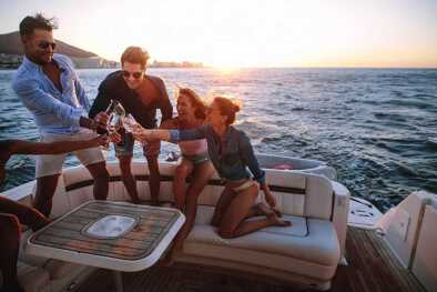 Grupo de jóvenes sentados en la parte trasera de un yate y brindando bebidas. Jóvenes haciendo una fiesta en barco al atardecer.