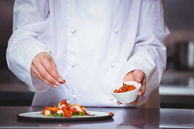 Chef che cosparge di spezie un piatto in una cucina commerciale Chef che cosparge di spezie un piatto in una cucina commerciale
