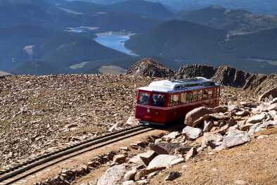 Vagón del Pikes Peak Cog Railway bajando desde la cima de la montaña Pikes Peak en Colorado en una soleada mañana de verano con las montañas y el lago en la distancia