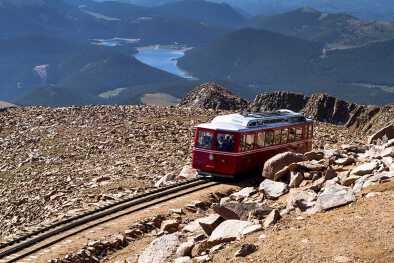 Vagón del Pikes Peak Cog Railway bajando desde la cima de la montaña Pikes Peak en Colorado en una soleada mañana de verano con las montañas y el lago en la distancia Vagón del Pikes Peak Cog Railway bajando desde la cima de la montaña Pikes Peak en Colorado en una soleada mañana de verano con las montañas y el lago en la distancia