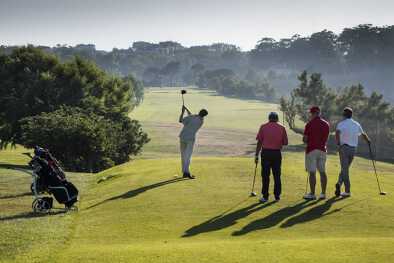 Eine Gruppe von Golfern beobachtet einen Golfer beim Abschlag im Sonnenschein Eine Gruppe von Golfern beobachtet einen Golfer beim Abschlag im Sonnenschein