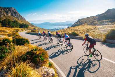 Eine Gruppe von Radfahrern fährt bergab in einer malerischen Seenlandschaft Eine Gruppe von Radfahrern fährt bergab in einer malerischen Seenlandschaft