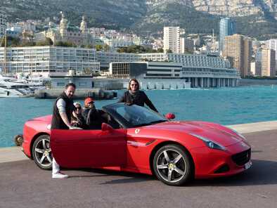 two guys pose in front a two ferrari