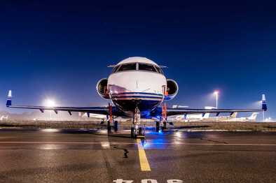Vista frontal de un jet privado que espera en una pista de aterrizaje por la noche