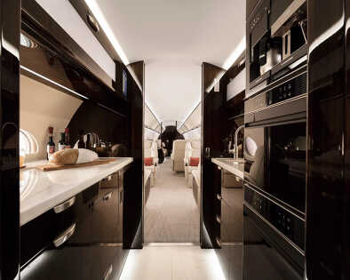 Vista del pasillo central de la cabina del Gulfstream G600: cocina moderna con hornos, microondas y otros equipos de alta gama para un confort de viaje óptimo.