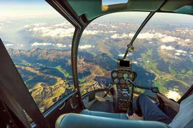 Cabina de helicóptero volando sobre paisajes montañosos y cielo nublado, con brazo piloto conduciendo en cabina. Espectacular vista aérea de los Alpes. Cabina de helicóptero volando sobre paisajes montañosos y cielo nublado, con brazo piloto conduciendo en cabina. Espectacular vista aérea de los Alpes.