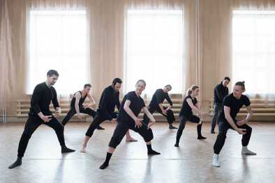 Tänzer in schwarzer Kleidung proben in einem großen, luftigen Studio