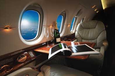 Luxuriöse Innenausstattung von einem modernen Business-Jet mit einer Flasche Champagner und Blick auf den Himmel und Wolken durch das Fenster